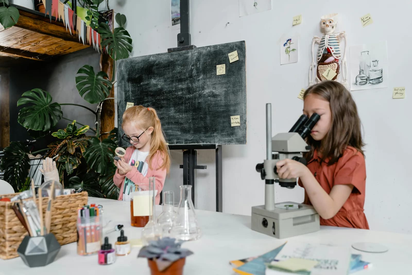 Two primary school students using a microscope and magnifying glass in a science classroom